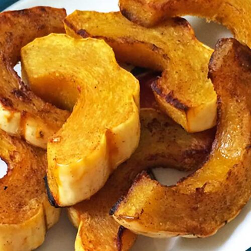 Roasted delicata squash slices with golden, caramelized edges on a white plate — an easy and healthy delicata squash recipe.