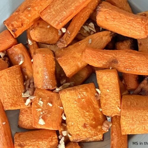 Roasted carrots with honey and walnuts on a blue-grey plate on a dark wood table