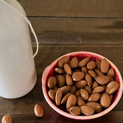 Homemade almond milk in glass bottle with bowl of raw almonds on wooden table