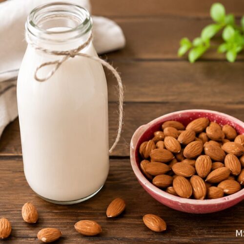 Homemade almond milk in a glass bottle beside a bowl of raw almonds on a rustic wooden table