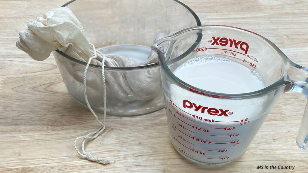 Straining homemade almond milk through nut milk bag into measuring cup