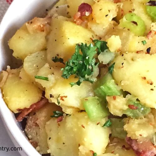 Egg-free sweet potato salad with turkey bacon, celery, and fresh parsley in a white bowl