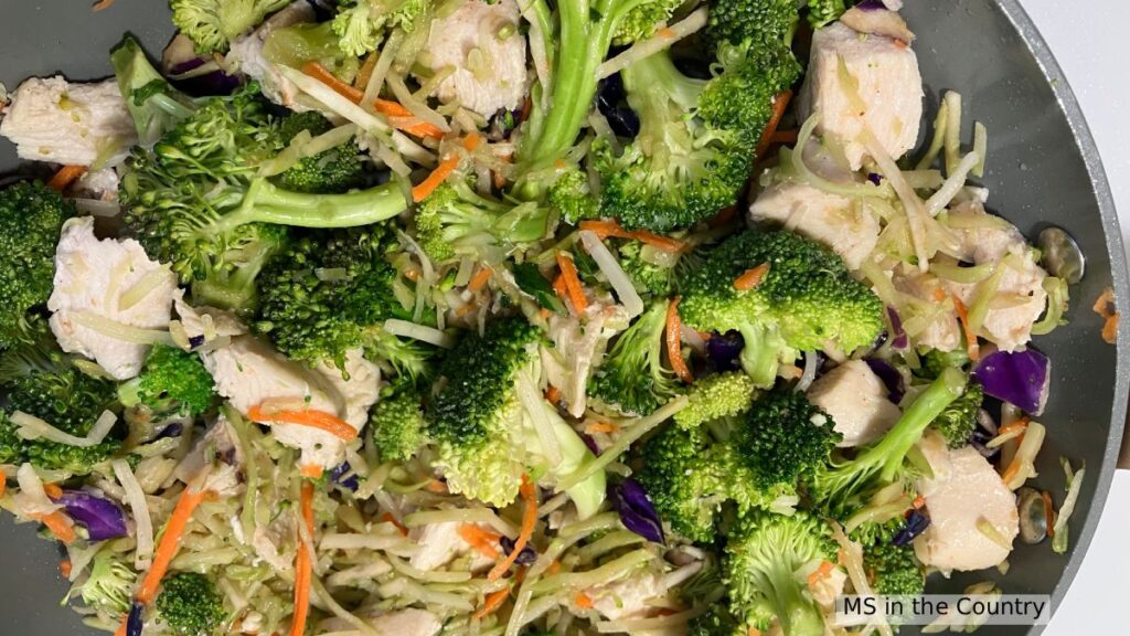 3 ingredient chicken and broccoli stir fry cooking in a pan with broccoli florets, shredded carrots, and purple cabbage