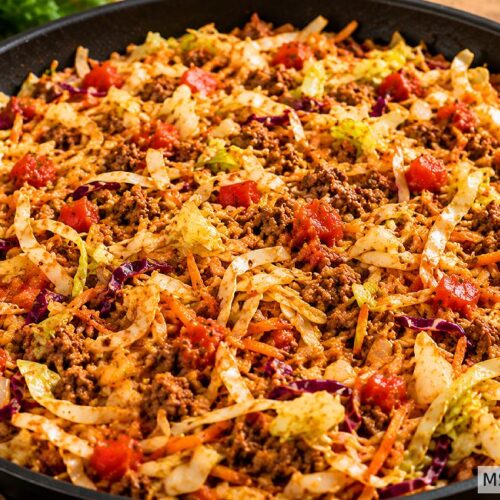 Healthy sloppy Joe recipe with coleslaw mix, ground beef, and diced tomatoes cooking in a black skillet