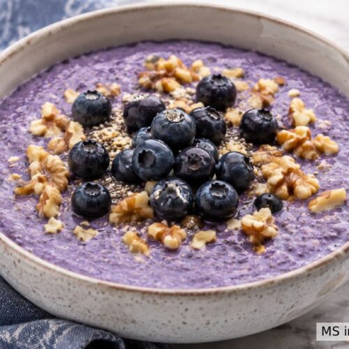 Blueberry chia pudding in a speckled bowl topped with fresh blueberries, chopped walnuts, and chia seeds