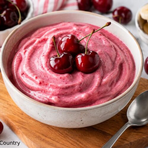 Cherry nice cream made with frozen dark cherries and banana in a white bowl on a wooden board