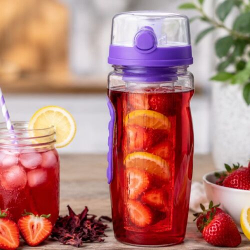 Strawberry lemonade herbal cooler in a purple fruit infuser bottle and mason jar with fresh strawberries and lemon slices