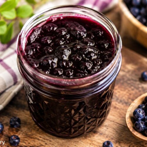 Homemade wild huckleberry jam in a glass jar on a rustic wooden table.
