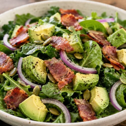 Bacon Avocado Salad made with mixed greens, creamy avocado, crispy turkey bacon, red onion, pumpkin seeds, and a fresh lemon olive oil dressing served in a rustic bowl.